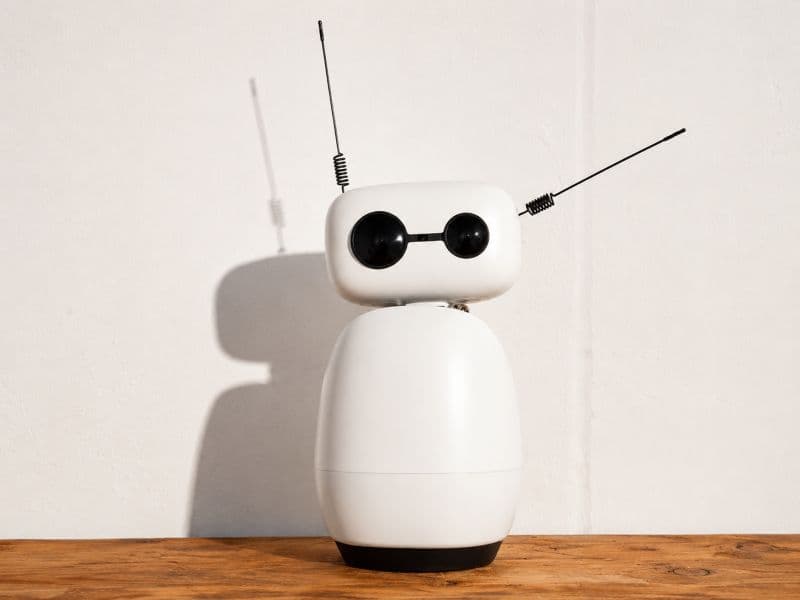 Robot blanco de escritorio con dos antenas sobre una repisa de madera